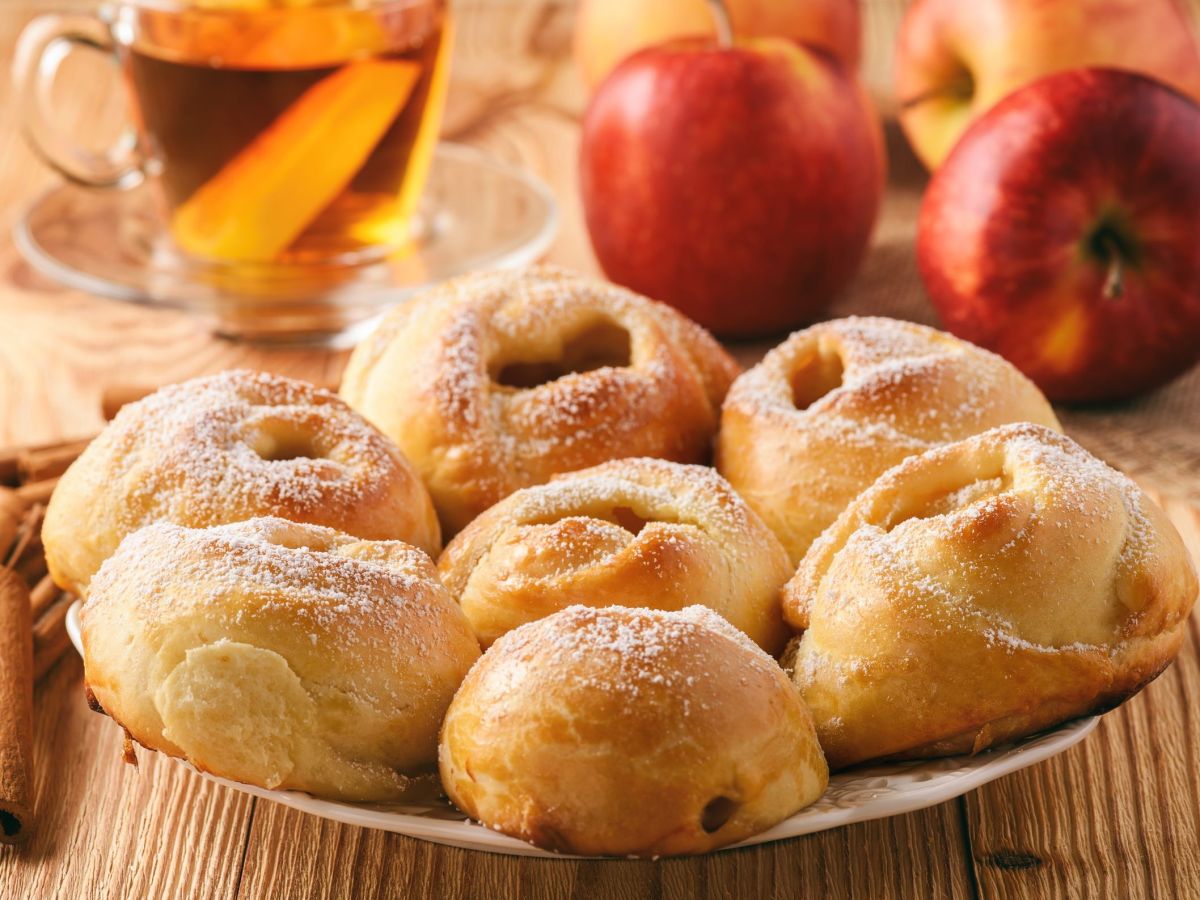 Ein Teller voller Bratapfel-Brötchen. Im Hintergrund liegen ein Äpfel und daneben steht eine Teetasse.