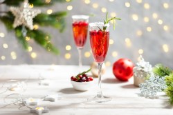 2 Gläser Cranberry Mimosas mit Cranberrys und Rosmarin garniert, im Hintergrund weihnachtliche Deko.