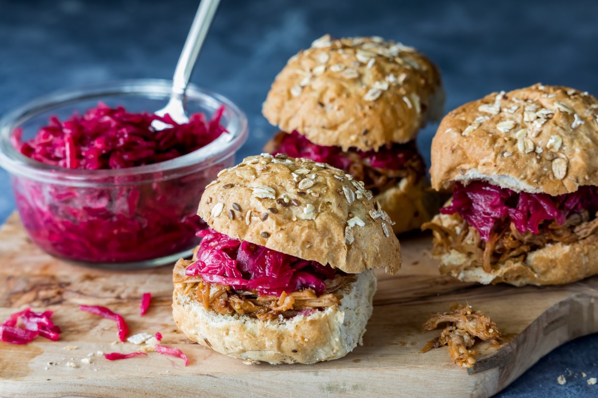 3 kleine Rotkohl-Gänse-Burger auf einem Brett, auf dem auch eine Glasschüssel mit Rotkohl steht.