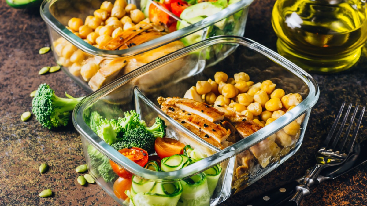 2 Glascontainer mit gesundem, vorbereiteten Essen. Daneben eine Gabel und eine kleine Glaskaraffe mit Öl.