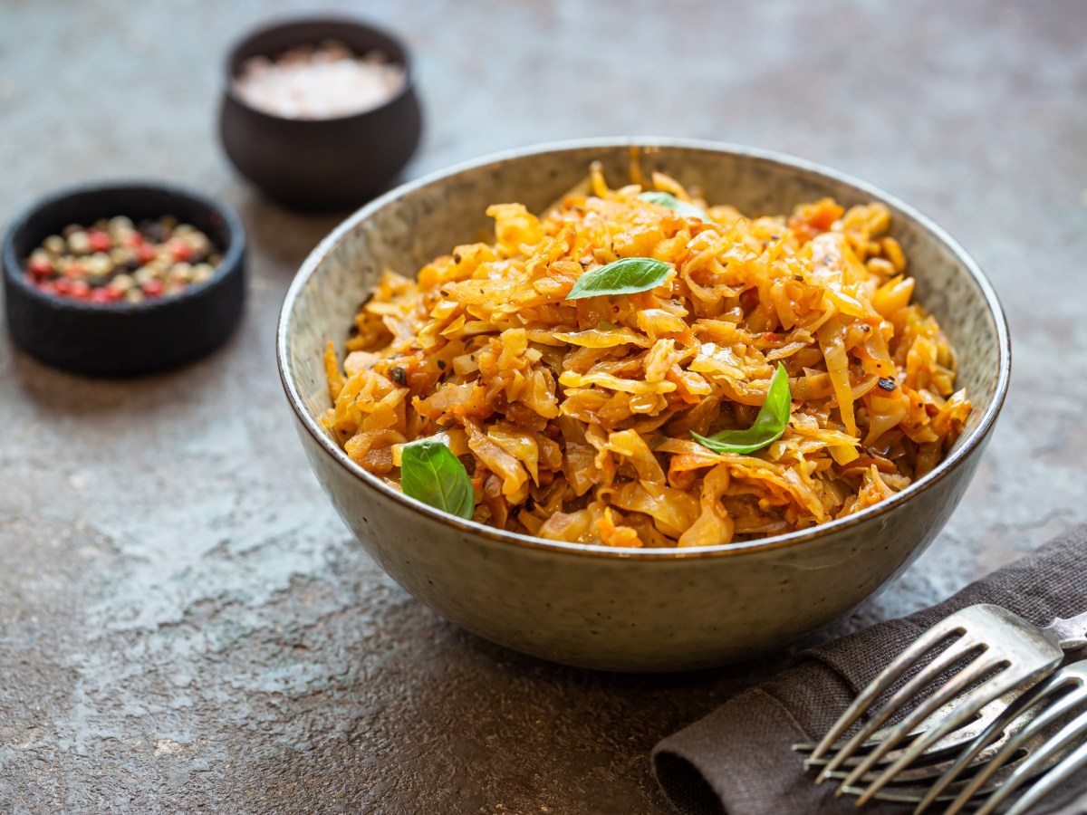 Eine Schüssel Schichtkohl mit Hackfleisch und Kartoffeln, daneben Besteck auf einem Geschirrtuch sowie Gewürzschalen.