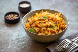 Eine Schüssel Schichtkohl mit Hackfleisch und Kartoffeln, daneben Besteck auf einem Geschirrtuch sowie Gewürzschalen.