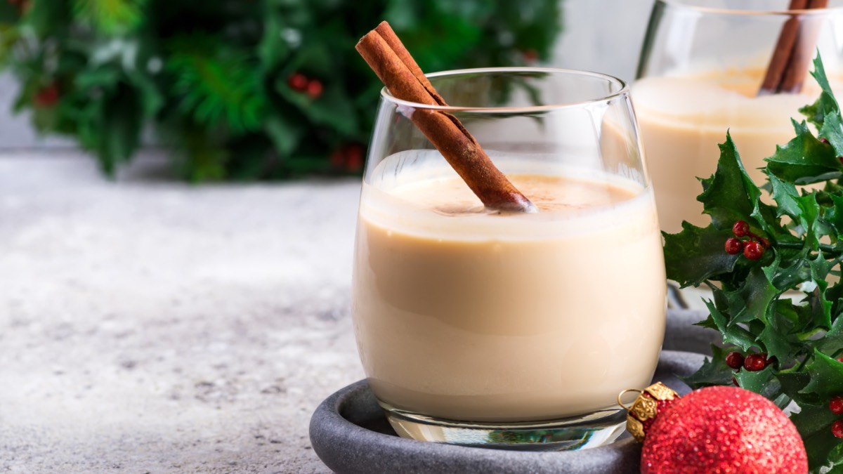 Ein Glas mit Spekulatius-LikÃ¶r, in dem eine Zimtstange steckt. Im Hintergrund steht ein weiteres Glas, einige Zweige Stechpalme und eine Christbaumkugel.