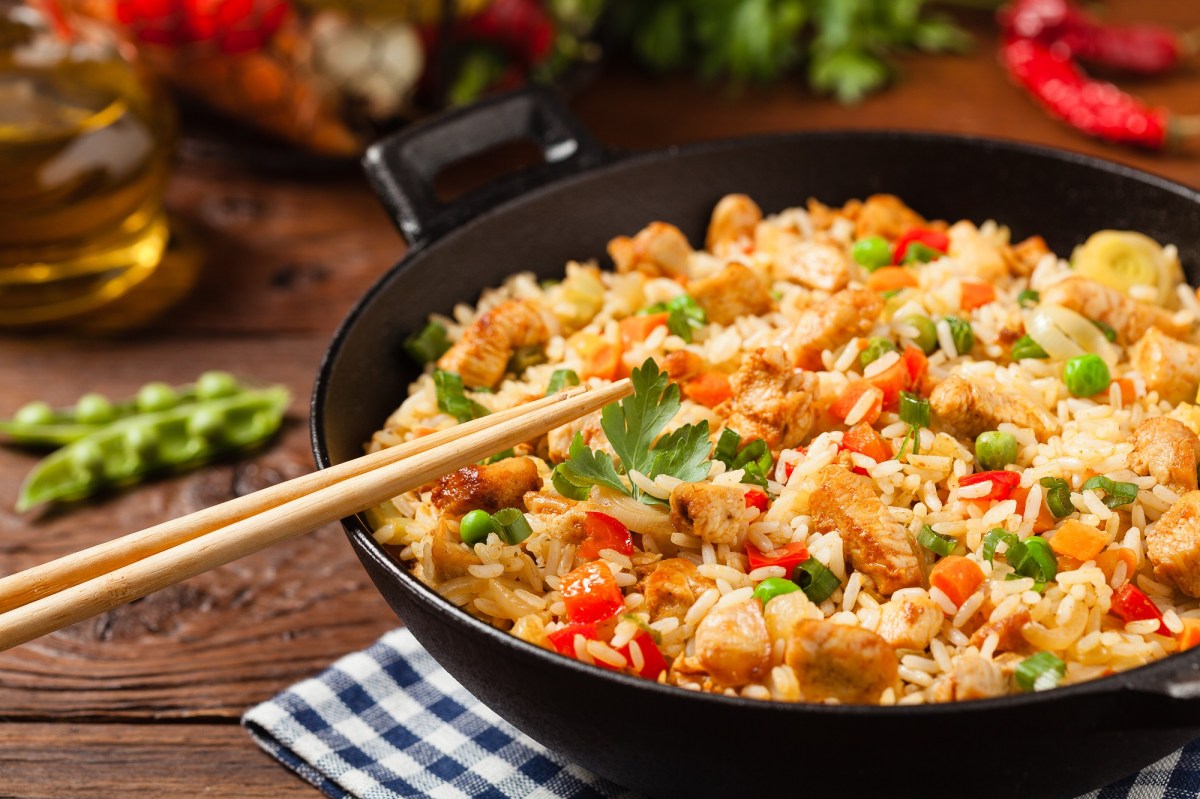 Asiatischer Bratreis mit Gemüse und Tofu in einer Pfanne, darauf liegen Essstäbchen.