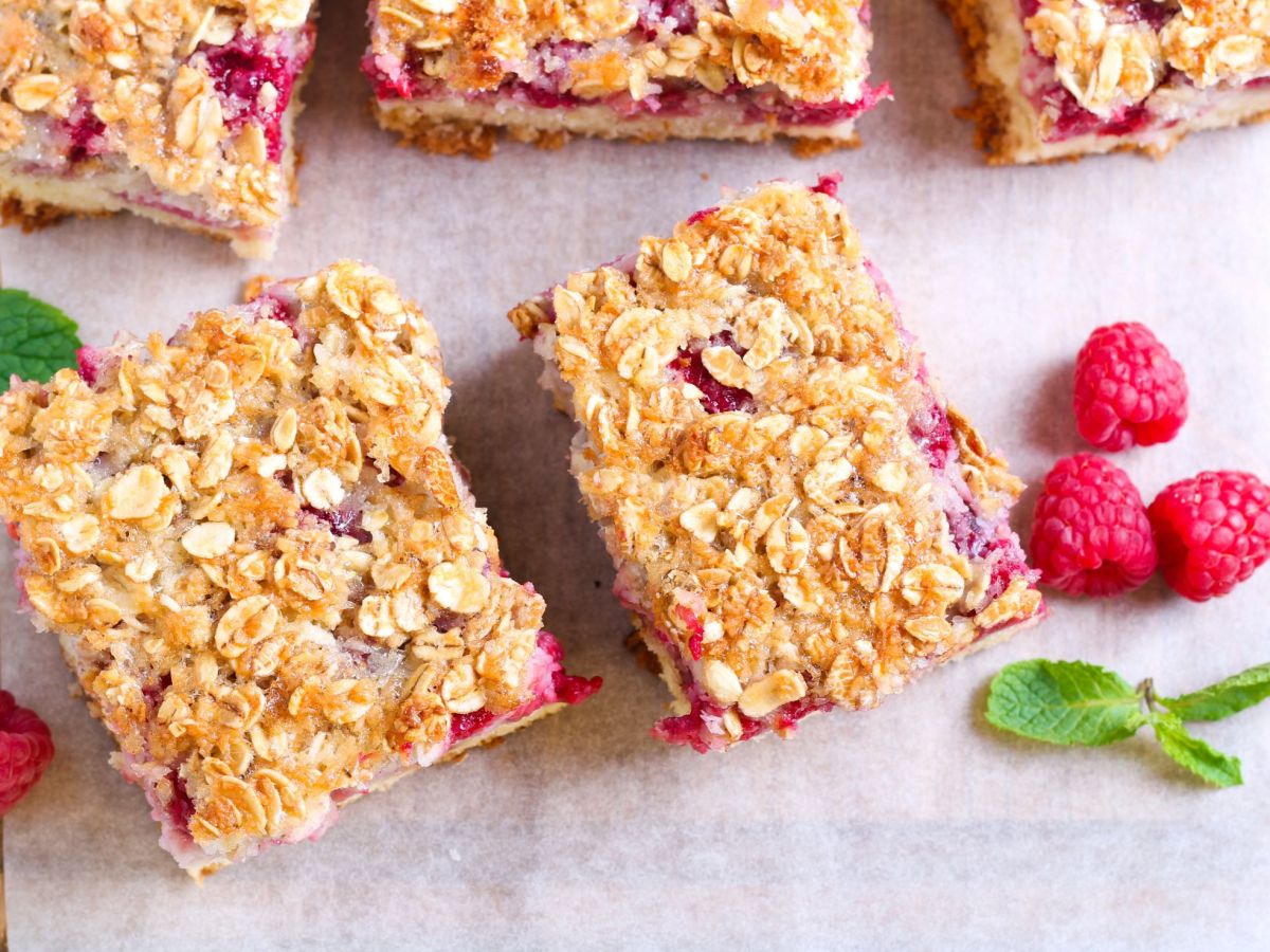 Bananen-Himbeer-Riegel ohne Zucker auf einem Pergamentpapier, einige Himbeeren liegen als Dekoration daneben.