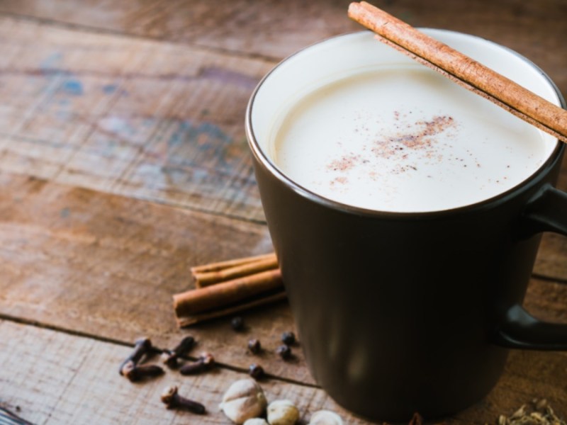 Eine Tasse Chai Latte, auf der eine Zimtstange am Rand liegt.