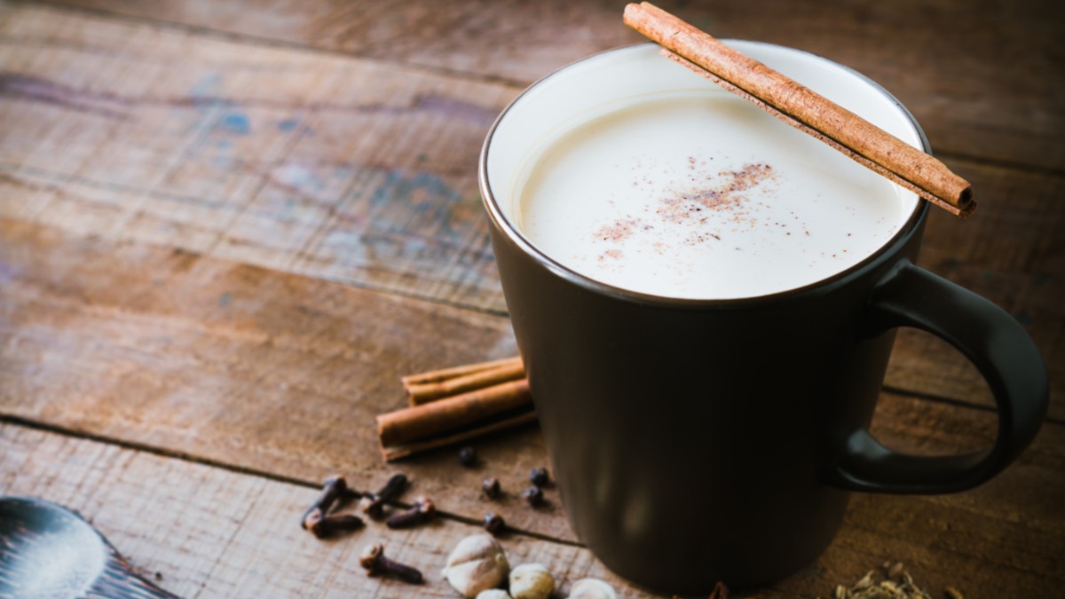 Eine Tasse Chai Latte, auf der eine Zimtstange am Rand liegt.