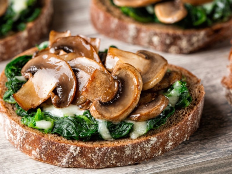 Mehrere Portionen Champignon-Bruschetta mit Ricotta und frischen Kräutern.