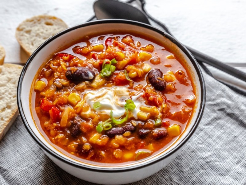 Eine Schüssel mit Chili sin Carne auf einer Stoffserviette. Daneben liegen Brotscheiben und ein Löffel.