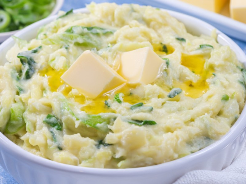 Eine Schüssel mit Colcannon. Daneben liegen ein Löffel und mehrer schalen mit Zutaten.