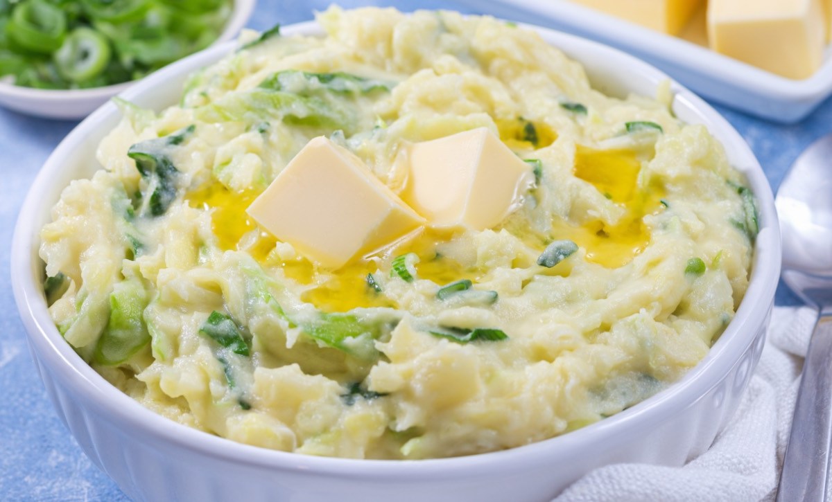 Eine Schüssel mit Colcannon. Daneben liegen ein Löffel und mehrer schalen mit Zutaten.