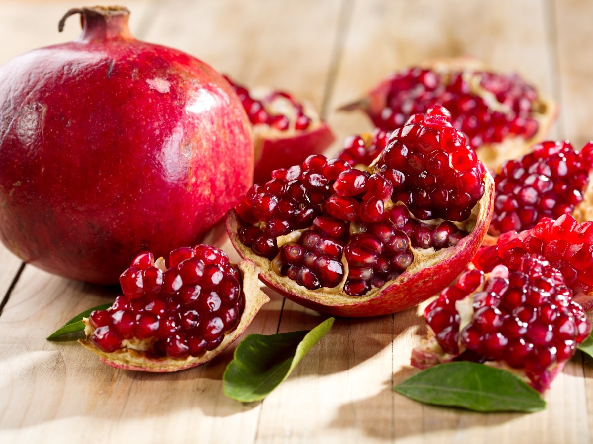 Granatapfel entkernen: ein ganzer und ein geöffneter Granatapfel auf Holz.