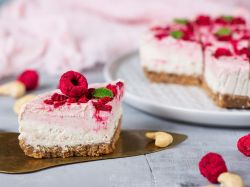 Ein Stück Himbeerwolke liegt auf einem Brett. Im HIntergrund ist der angeschnittene Kuchen zu sehen.