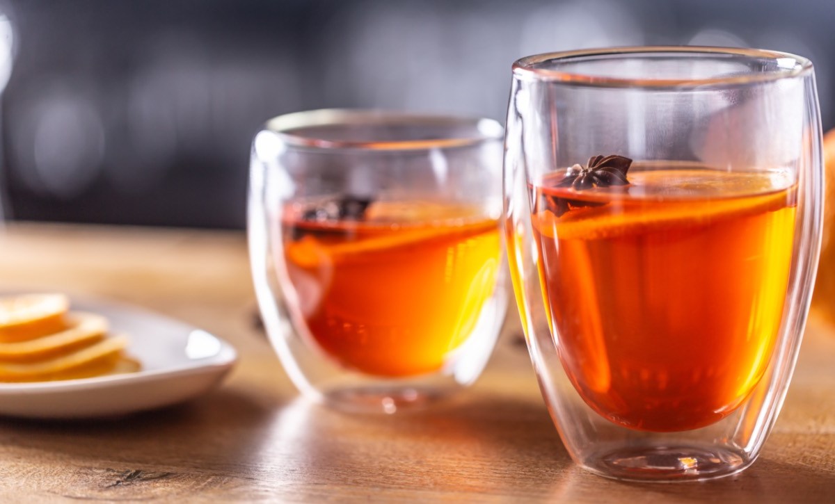 2 Gläser Hot Aperol mit Orangenscheiben und winterlichen Gewürzen. Daneben steht eine schale mit Orangenscheiben.