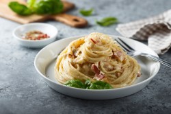 Italienische Spaghetti Carbonara auf einem weißen Teller, garniert mit Basilikum.