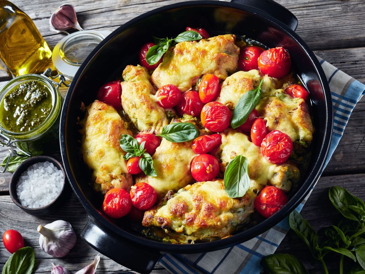 Mozzarella-Hähnchen mit Tomaten in einer Pfanne serviert. Außen herum stehen Salz, Essig und Öl als Deko.