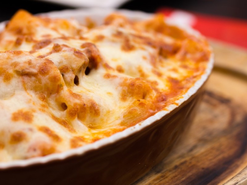 Eine Auflaufform mit Rigatoni al forno auf einem Holzbrett.