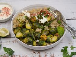 Rosenkohlsalat mit Couscous und Dressing. Dressing, Limette und Kräuterblättchen liegen daneben.