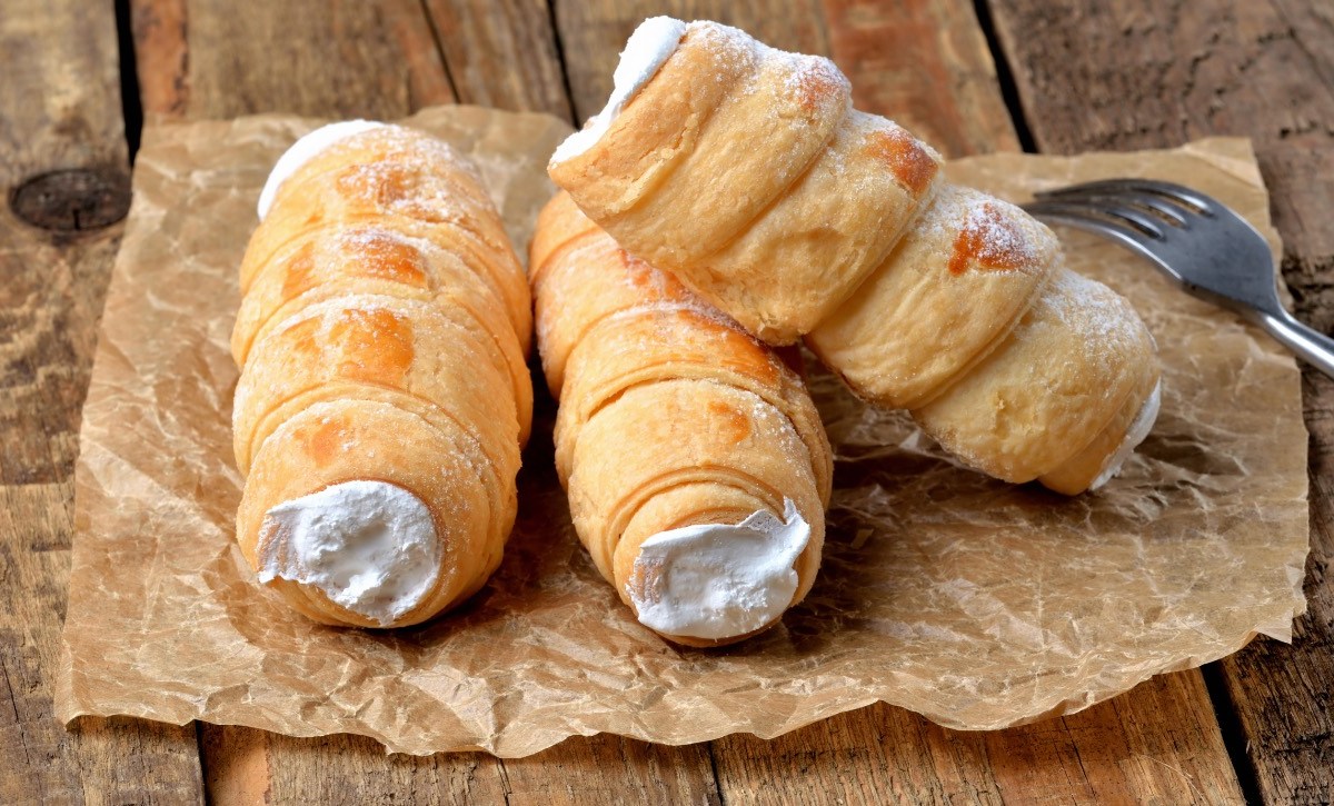 Drei Schaumrollen mit Vanillecreme auf einem Stück Backpapier.