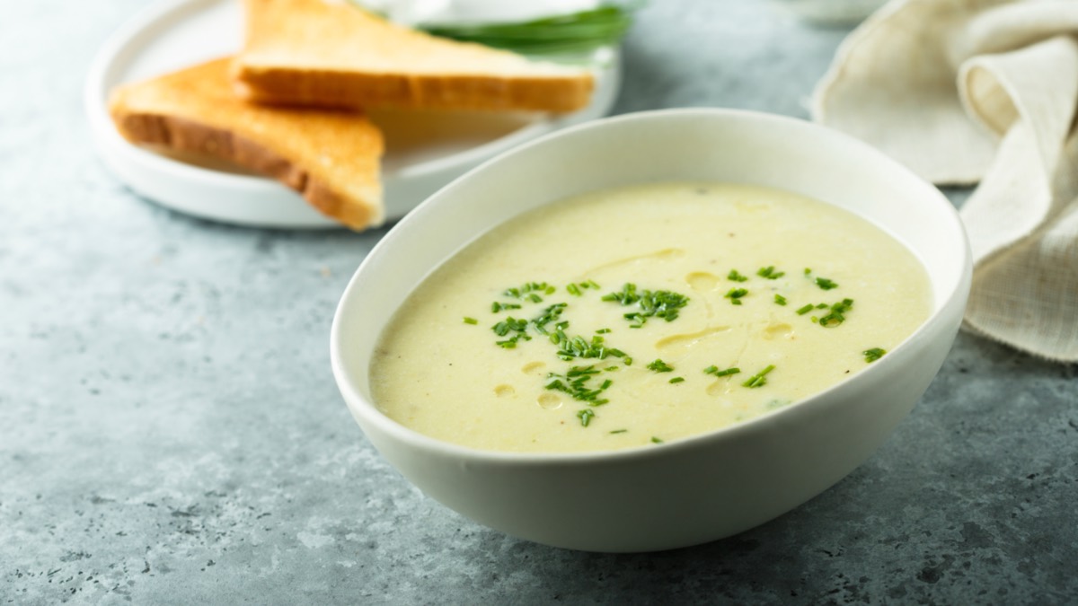 Eine Schüssel Schwarzwurzelsuppe mit frischem Schnittlauch. Daneben ein Teller mit 2 halbierten Toastscheiben.