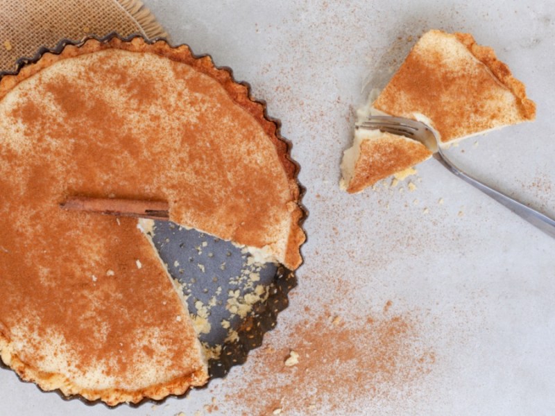 Eine südafrikanische Milchtarte in der Form, von oben fotografiert. Ein Stück Tarte liegt samt Gabel daneben.