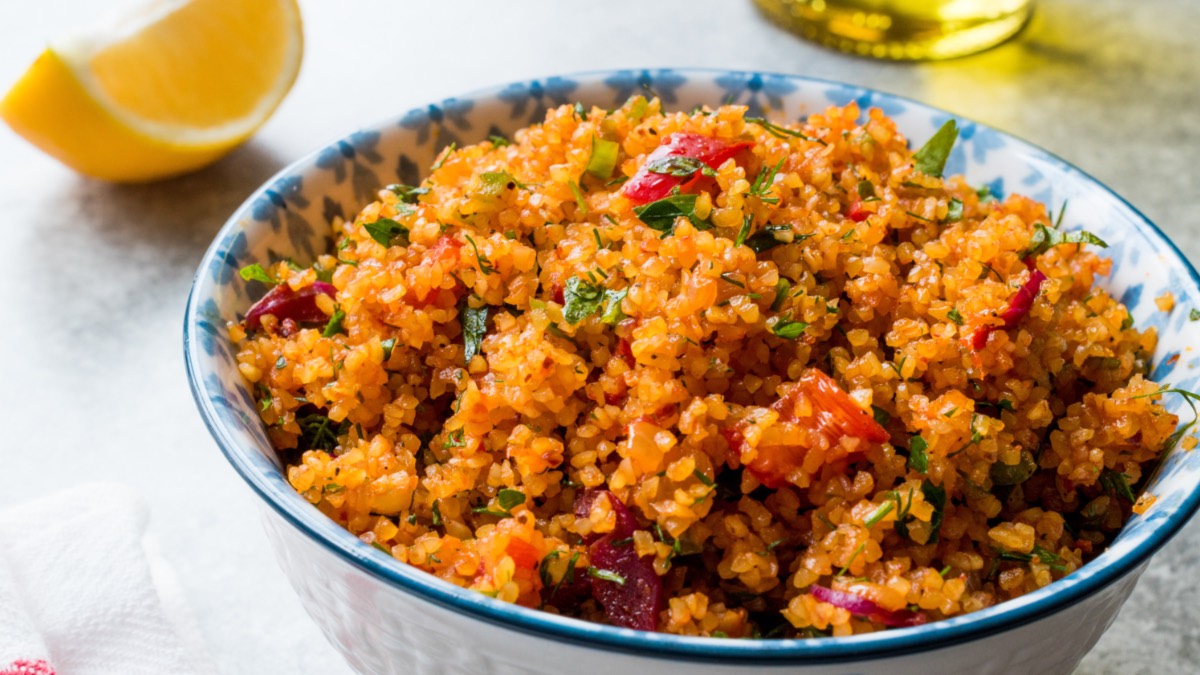 Eine Schüssel mit türkischem Bulgursalat. Daneben liegt eine Zitronenspalte.