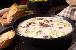 Eine Schüssel vegane Käse-Lauch-Suppe mit Hack, daneben geröstete Baguettescheiben.