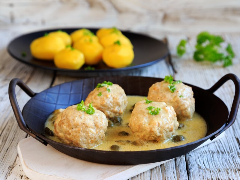 Vegane Königsberger Klopse in einer gusseisernen Pfanne mit Kapernsauce, dazu Salzkartoffeln.