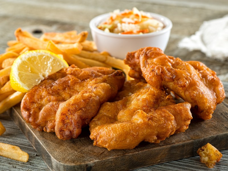 Panieren ohne Ei: frittiertes Essen, das mit veganer Panade zubereitet wurde, daneben Pommes und eine Schale mit Dip.