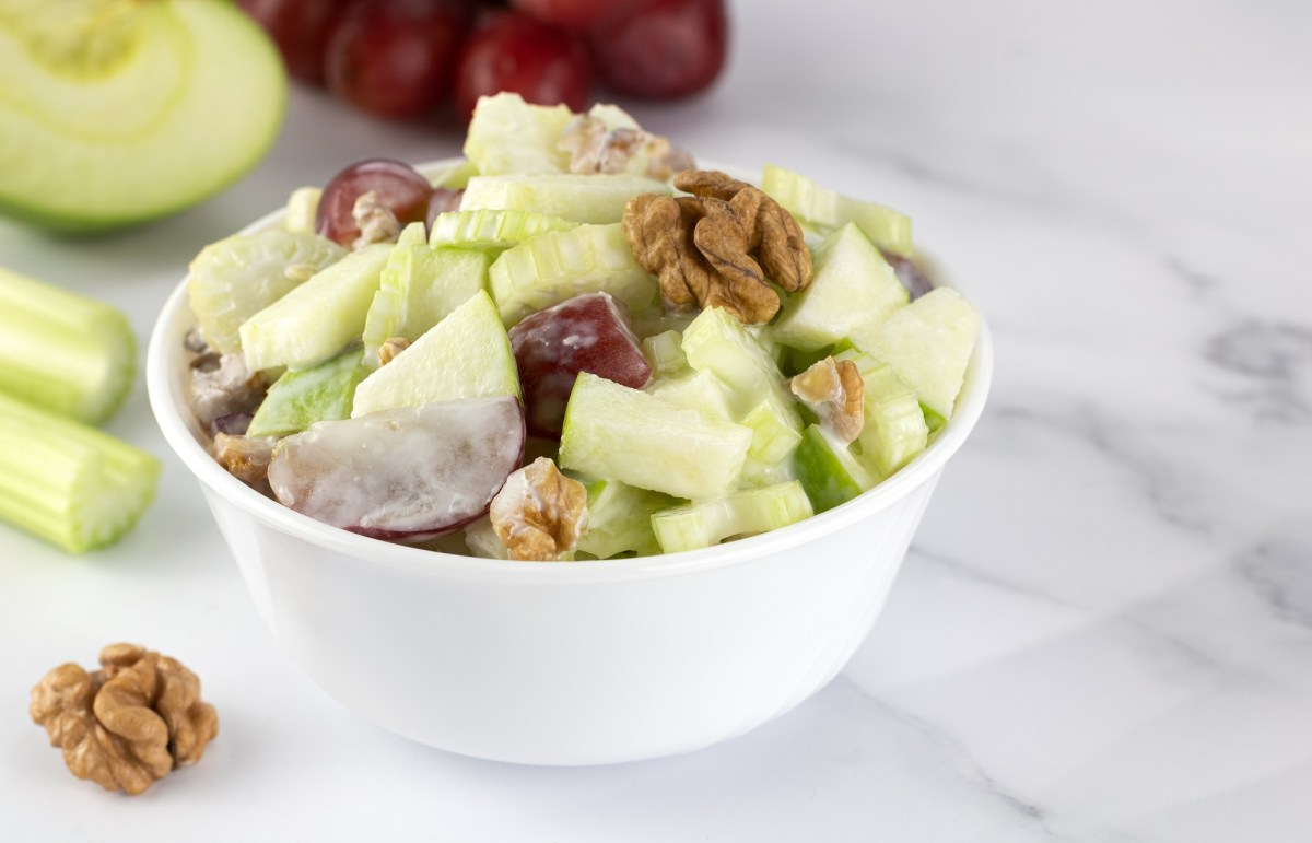 Grob geschnittener Waldorfsalat in einer weißen Schale auf einem Marmortisch.