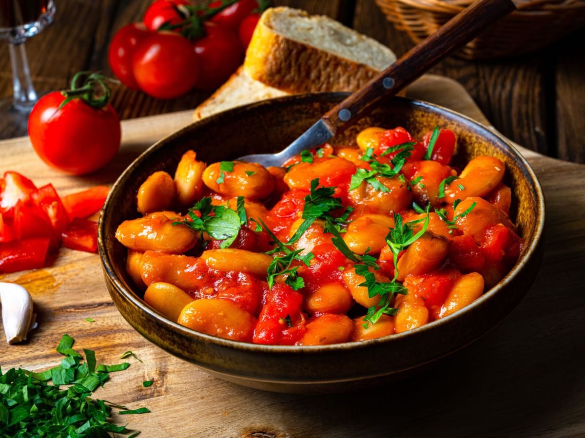 Weiße Bohnen-Pfanne, serviert in einer Pfanne. Tomaten und andere Kräuter liegen als Dekoration daneben.