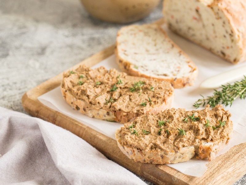 Zwei Brotscheieben mit Zwiebelbutter bestrichen auf einem Brett, auf dem auch das angeschnittene Brot liegt.