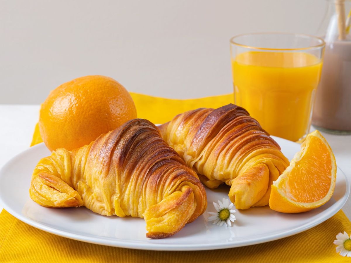 Zwei schnelle Brioches, auf einem Teller angerichtet. Auf dem Teller liegt eine Orangenscheibe als Deko und ein Glas O-Saft liegt im Hintergrund.