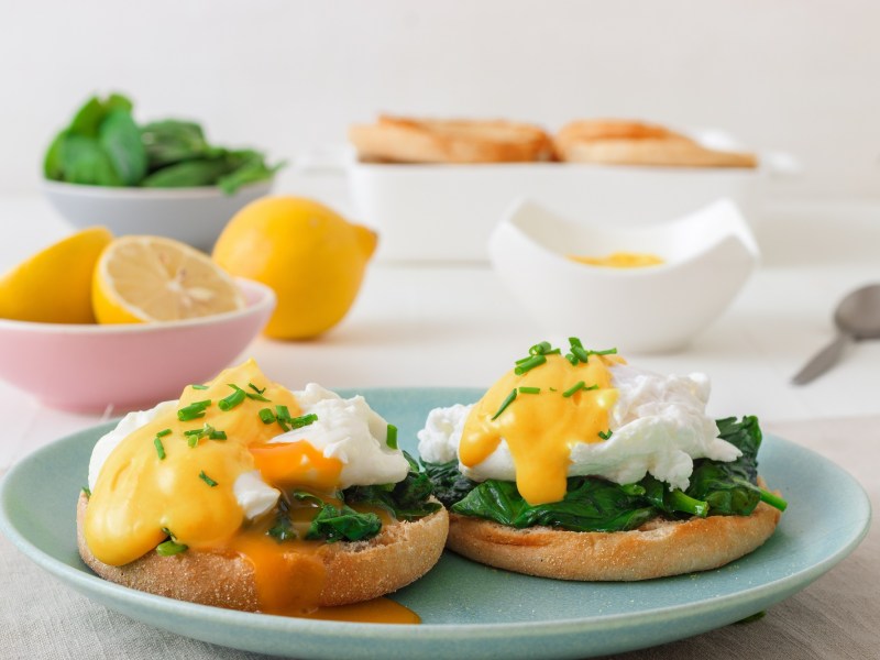 Eggs Florentine aus Spinat mit Käsesoße auf einem blauen Teller.