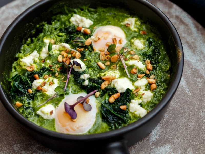 Pfanne mit grünem Shakshuka, Pinienkernen und pochierten Eiern