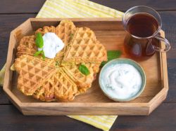 Karottenwaffeln liegen auf einem Stapel auf einem Tablett, ein Schälchen mit Dip steht daneben. Ebenso wie ein Gläschen Tee.