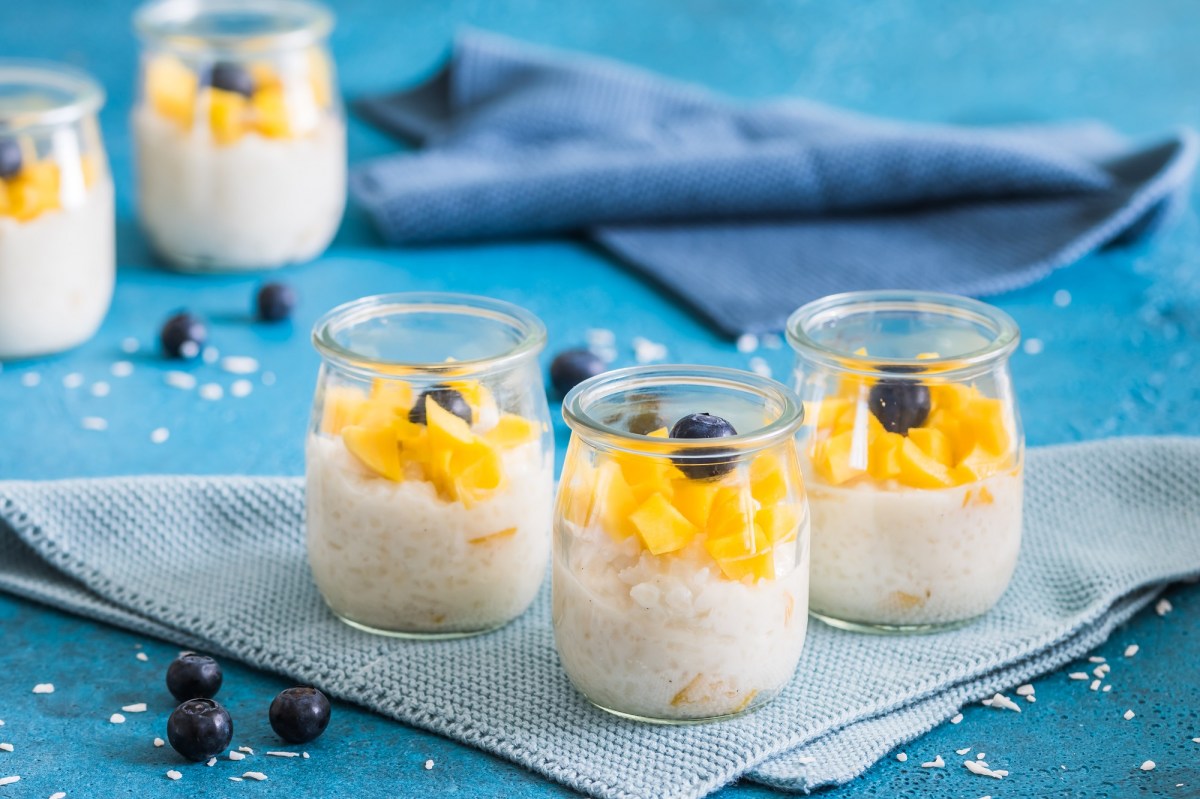 Fünf Gläser gefüllt mit Reis und Mangos auf einer blauen Tischdecke