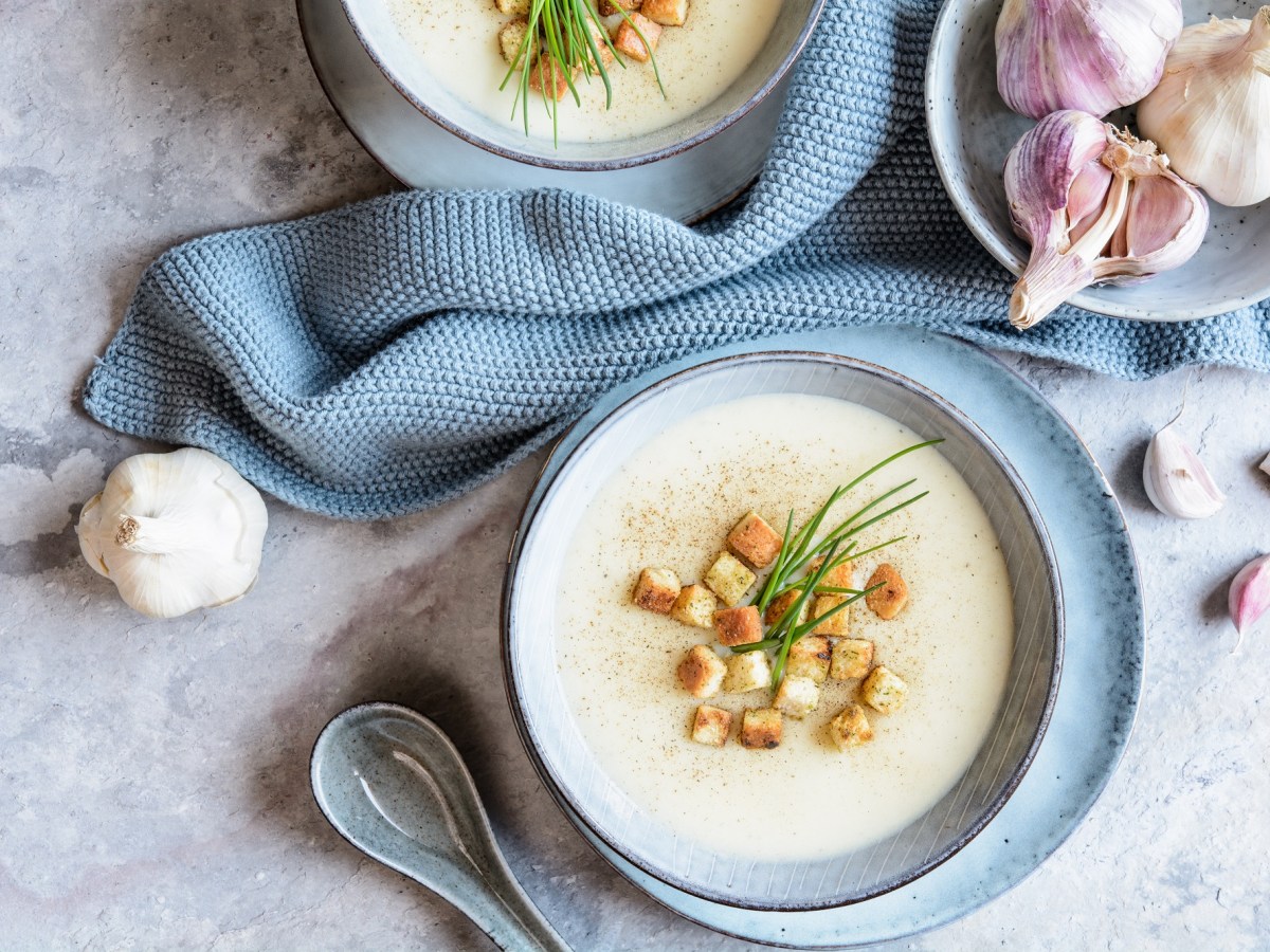 Schale Knoblauchsuppe mit Coutons auf einem Tisch mit blauem Tischtuch.