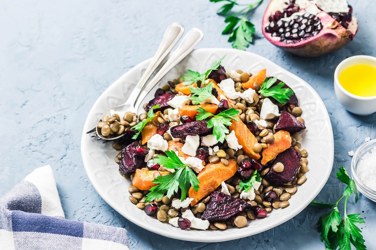 Linsensalat mit Wintergemüse auf einem weißen Teller. Daneben Petersilie und eine Schale Olivenöl.