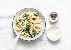 Ein Teller Nudeln mit Spinat-Käse-Soße mit Gabel in der Draufsicht, daneben je eine Schüssel mit Pfeffer und geriebenem Parmesan.