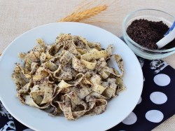 Pasta mit Mohn auf einem weißen Teller auf einem schwarz-weißen Tischuntersetzer. Daneben steht eine Schüssel mit Mohn-Topping.