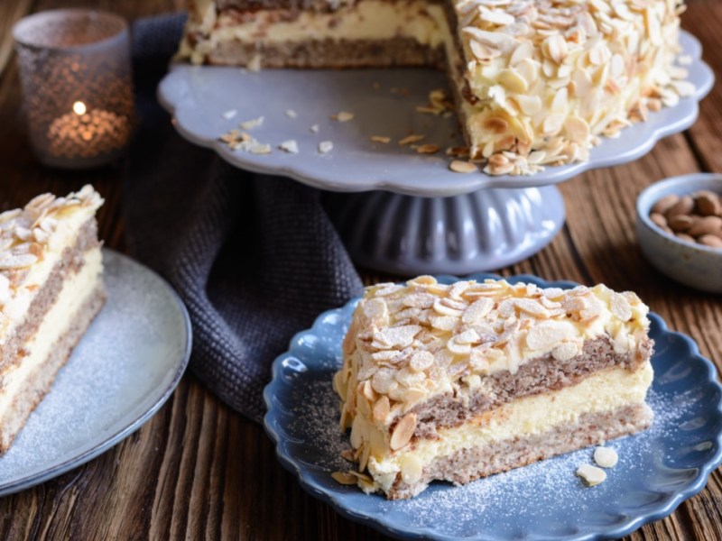 Zwei Stücke schwedische Mandeltorte auf Tellern im Vordergrund. Dahinter die restliche Torte auf einer Kuchenplatte.