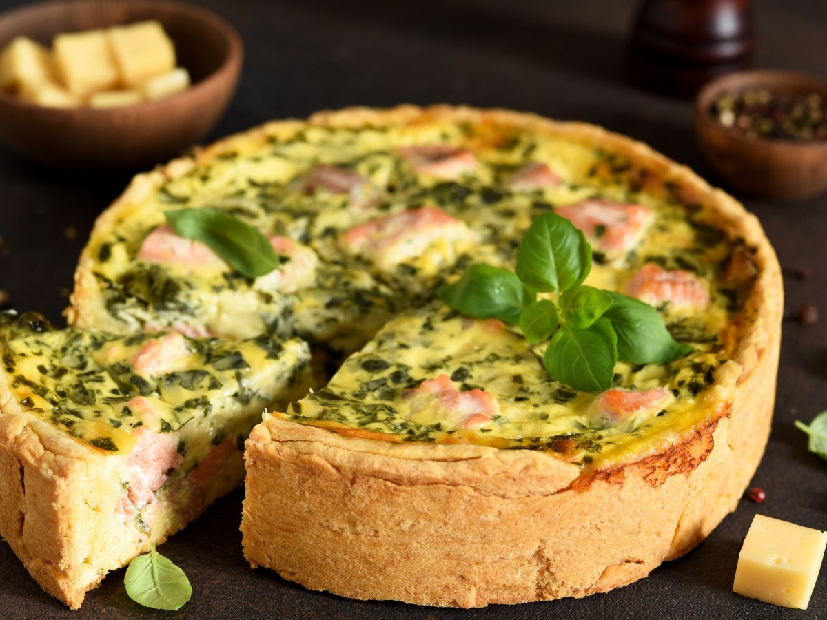 Spinat-Lachs-Quiche mit Basilikum dekoriert auf einem dunklen Untergrund.