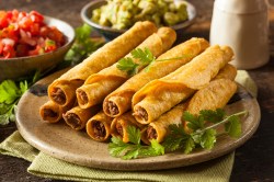 Taquitos mit Hackfleischfüllung auf einem beigen Teller, garniert mit Koriander und serviert mit Tomaten-Salsa, Guacamole und Sour Cream.