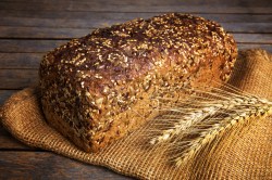 Ein Laib Vollkornbrot mit verschiedenen Saaten auf einem Mehlsack. Daneben zwei Getreideähren.