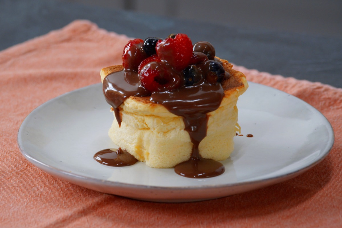 Ein fluffiger Würfelkuchen mit Schokosoße und frischen Beeren auf einem Teller.