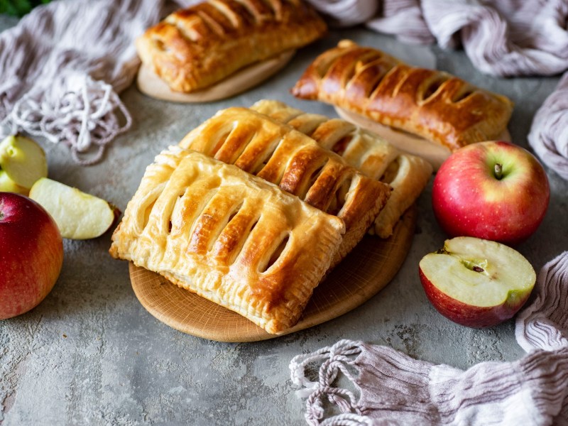 4 Apfel-Quark-Taschen auf einem Teller, drumherum ganze und halbierte Äpfel.