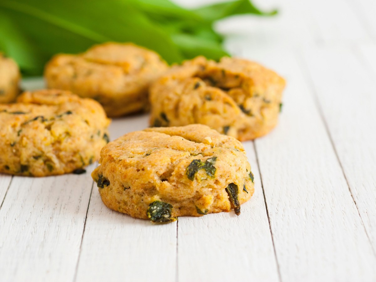 Mehrere Bärlauch-Scones auf weißem Holz, dahinter unscharf frischer Bärlauch.