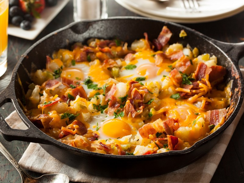 Gusseiserne Pfanne mit Frühstückspfanne mit Ei und Speck auf dunklem Tisch