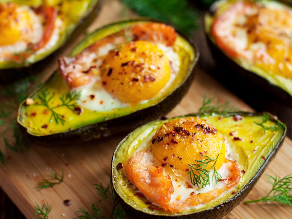 Ein Holzbrett mit gebackenen Avocados mit Ei und Lachs